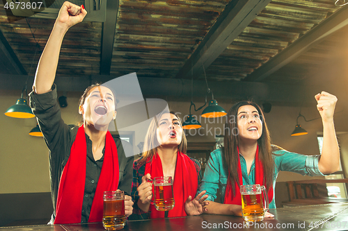 Image of Sport, people, leisure, friendship and entertainment concept - happy football fans or female friends drinking beer and celebrating victory at bar or pub