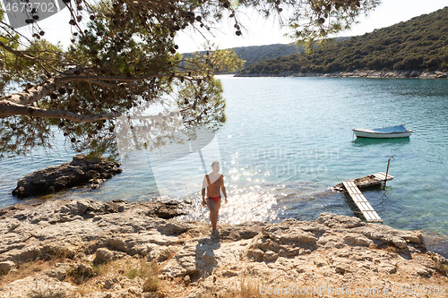 Image of Young sporty man wearing red speedos tanning and realaxing on wild cove of Adriatic sea on a beach in shade of pine tree