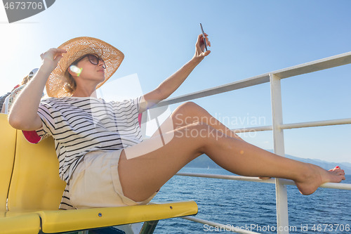 Image of Beautiful, romantic blonde woman taking selfie self portrait photo on summer vacations traveling by cruse ship ferry boat.