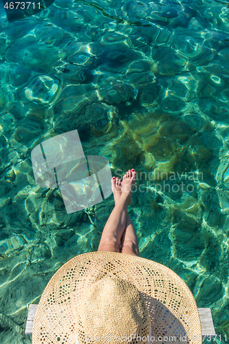 Image of Graphic image of top down view of woman wearing big summer sun hat relaxing on small wooden pier by clear turquoise sea