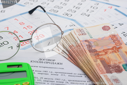Image of The purchase agreement contains a bundle of money, a calculator and glasses