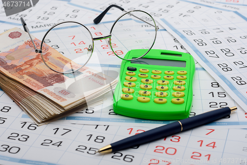 Image of Money, calculator, glasses and pen are on the calendar