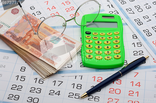 Image of Money, glasses, calculator and pen lie on the calendar