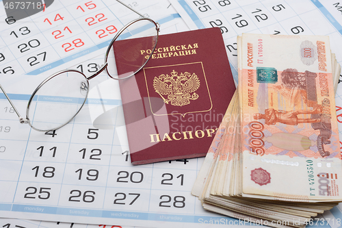 Image of Glasses, passport and a bundle of money are on the sheets of a wall calendar