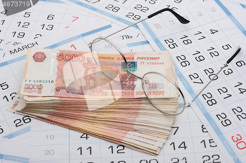 Image of Glasses lie on a bundle of five-thousandth Russian banknotes, background from calendar sheets
