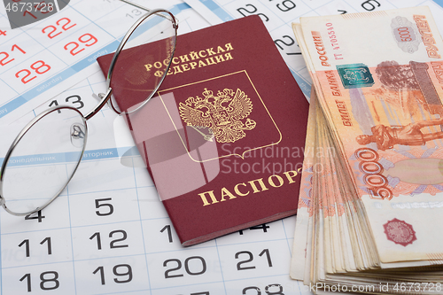 Image of The passport of the Russian Federation lies on the background of calendar numbers, next to it lies a bundle of money and glasses