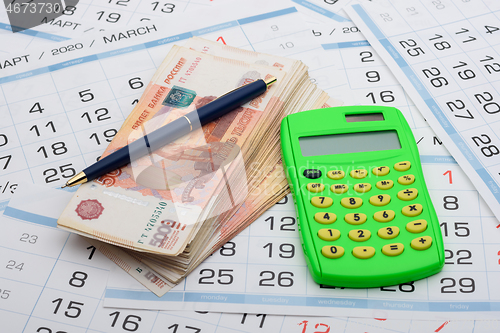 Image of There is a wad of money on the calendar, a calculator and a pen