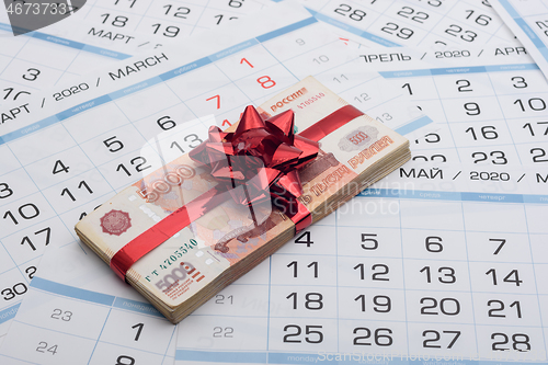 Image of A bundle of Russian five-thousandth bills with a red bow lies on a background from a calendar