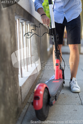 Image of Male user safely parking electric scooter and locking it to a fence. Eco friendly green modern urban mobility concept of sharing transportation with electric scooters for rent in Ljubljana, Slovenia