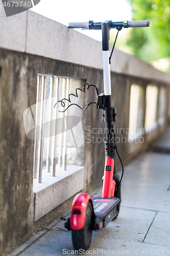 Image of Red electric scooter parked and safely chained to a fence. Eco friendly green modern urban mobility concept of sharing transportation with electric scooters for rent in Ljubljana, Slovenia