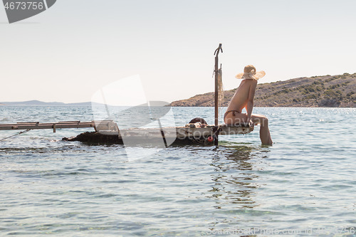 Image of View of unrecognizable woman wearing big summer sun hat tanning topless and relaxing on old wooden pier in remote calm cove of Adriatic sea, Croatia