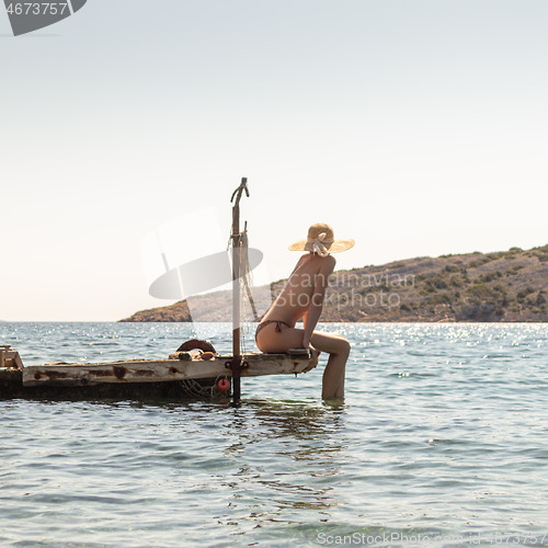 Image of View of unrecognizable woman wearing big summer sun hat tanning topless and relaxing on old wooden pier in remote calm cove of Adriatic sea, Croatia