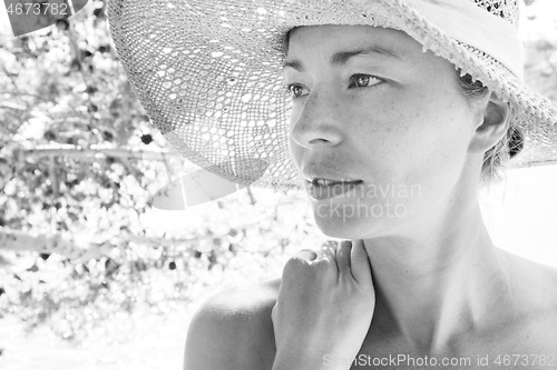 Image of Close up portrait of no makeup natural beautiful sensual woman wearing straw sun hat on the beach in shade of a pine tree in black and white.