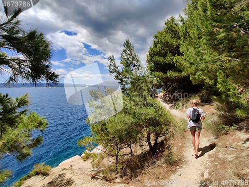 Image of Young active feamle tourist wearing small backpack walking on coastal path among pine trees looking for remote cove to swim alone in peace on seaside in Croatia. Travel and adventure concept