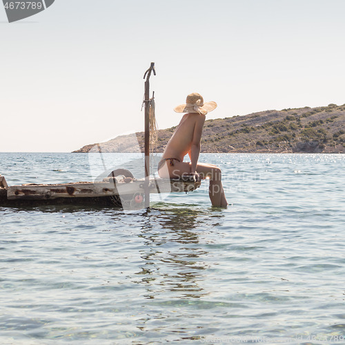 Image of View of unrecognizable woman wearing big summer sun hat tanning topless and relaxing on old wooden pier in remote calm cove of Adriatic sea, Croatia