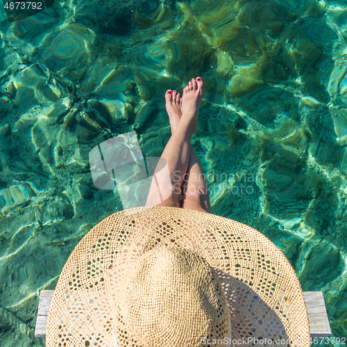 Image of Graphic image of top down view of woman wearing big summer sun hat relaxing on small wooden pier by clear turquoise sea