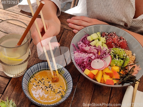 Image of Woman eating tasty colorful healthy natural organic vegetarian Hawaiian poke bowl using asian chopsticks on rustic wooden table. Healthy natural organic eating concept