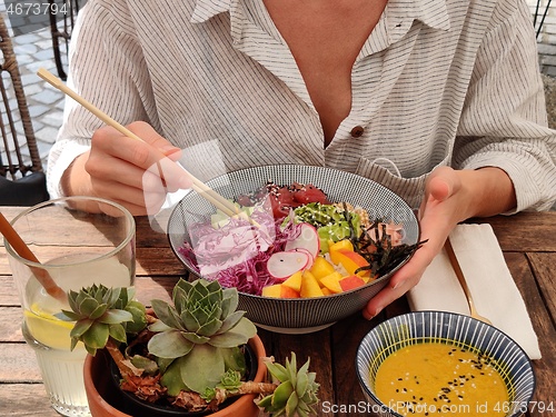 Image of Woman eating tasty colorful healthy natural organic vegetarian Hawaiian poke bowl using asian chopsticks on rustic wooden table. Healthy natural organic eating concept