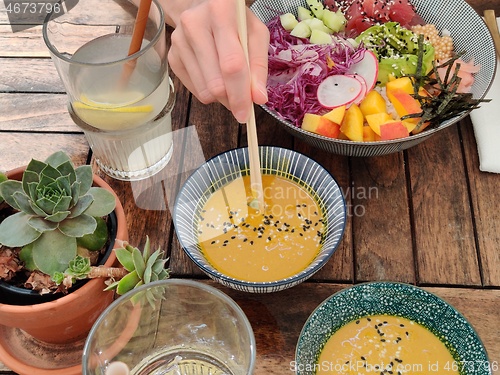 Image of Woman eating tasty colorful healthy natural organic vegetarian Hawaiian poke bowl using asian chopsticks on rustic wooden table. Healthy natural organic eating concept