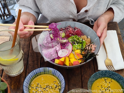 Image of Woman eating tasty colorful healthy natural organic vegetarian Hawaiian poke bowl using asian chopsticks on rustic wooden table. Healthy natural organic eating concept