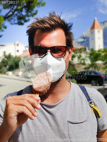 Image of Young guy on summer vacations wearing corona virus protective face mask not beeing able to lick ice cream bar