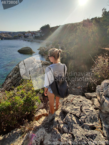 Image of Young active feamle tourist wearing small backpack walking on coastal path among pine trees enjoing beautiful costal view of Velo Zarace beach on Hvar island, Croatia. Travel and adventure concept