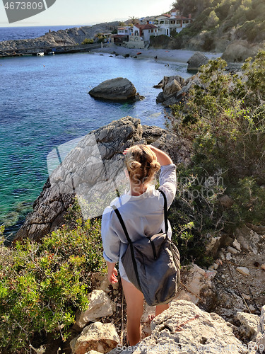 Image of Young active feamle tourist wearing small backpack walking on coastal path among pine trees enjoing beautiful costal view of Velo Zarace beach on Hvar island, Croatia. Travel and adventure concept