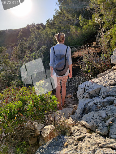 Image of Young active feamle tourist wearing small backpack walking on coastal path among pine trees looking for remote cove to swim alone in peace on seaside in Croatia. Travel and adventure concept