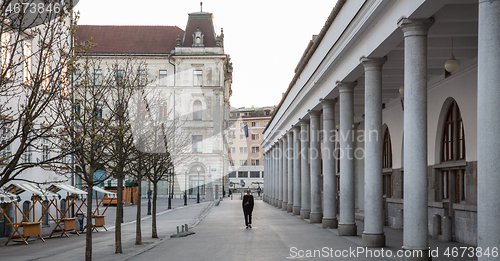 Image of Rear view of unrecognizable woman walking in empty old medieval Ljubljana city center during corona virus pandemic. Almost no people outside on streets