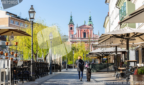 Image of Rear view of unrecognizable woman walking a dog in empty old medieval Ljubljana city center during corona virus pandemic. Empty bars and restaurants. Almost no people outside on streets