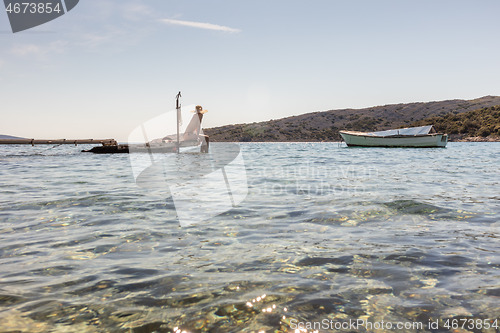 Image of View of unrecognizable woman wearing big summer sun hat tanning topless and relaxing on old wooden pier in remote calm cove of Adriatic sea, Croatia