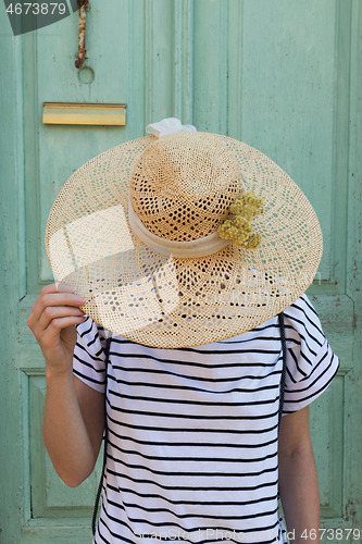 Image of Unrecognizable female tourist woman wearing big straw standing in front of vinatage turquoise wooden door at old Mediterranean town.