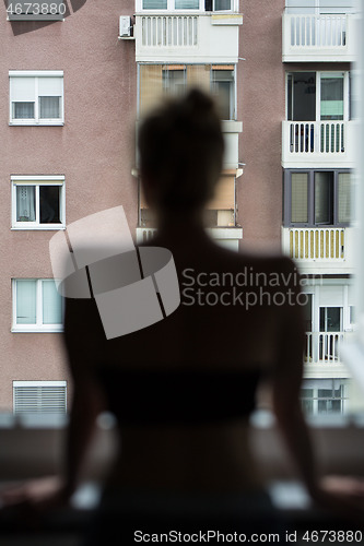 Image of Home quarantine and social distancing during covid pandemic. Silhouette of lonley caucasian woman standing by window, anxiously looking out. Coronavirus infection, pandemics, disease outbreaks