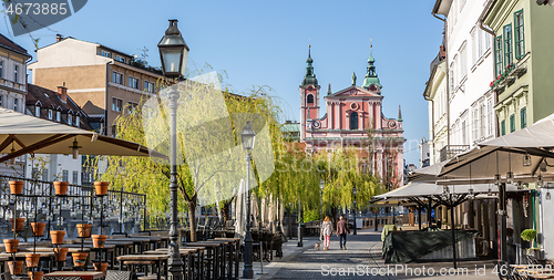 Image of Rear view of unrecognizable woman walking a dog in empty old medieval Ljubljana city center during corona virus pandemic. Empty bars and restaurants. Almost no people outside on streets