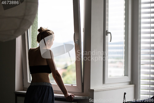 Image of Home quarantine and social distancing during covid pandemic. Silhouette of lonley caucasian woman standing by window, anxiously looking out. Coronavirus infection, pandemics, disease outbreaks