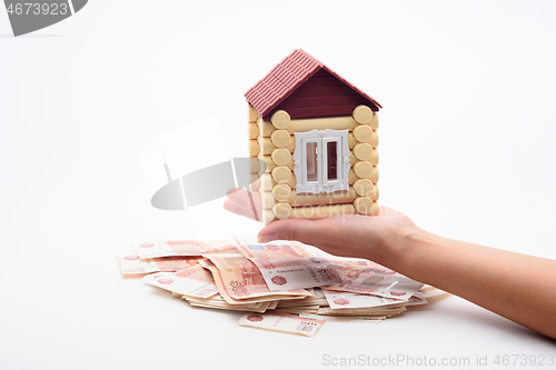 Image of A hand holds a house over a bundle of Russian five-thousandth bills