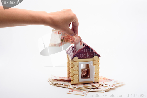 Image of Hand shoves a five thousandth bill into the roof of a house