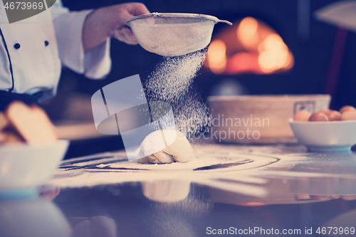 Image of chef sprinkling flour over fresh pizza dough