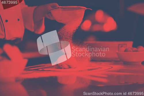 Image of chef sprinkling flour over fresh pizza dough