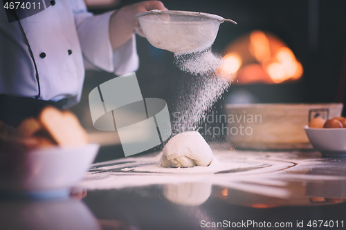 Image of chef sprinkling flour over fresh pizza dough