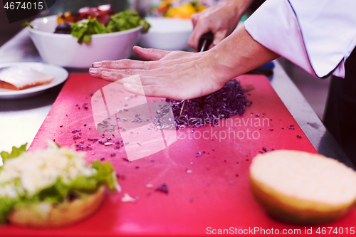 Image of chef hands cutting salad for burger