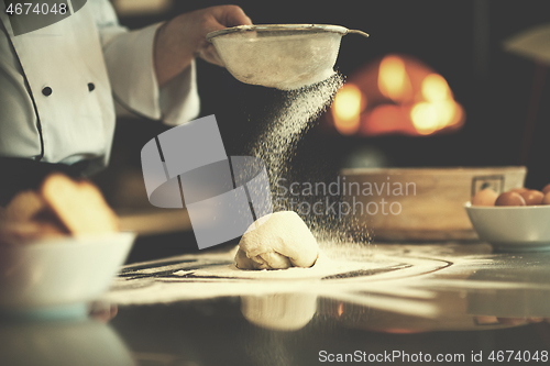 Image of chef sprinkling flour over fresh pizza dough