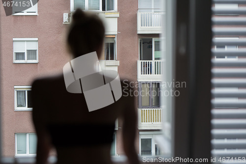 Image of Home quarantine and social distancing during covid pandemic. Silhouette of lonley caucasian woman standing by window, anxiously looking out. Coronavirus infection, pandemics, disease outbreaks