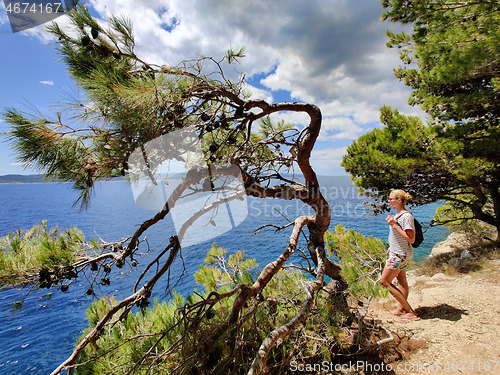 Image of Young active feamle tourist wearing small backpack walking on coastal path among pine trees looking for remote cove to swim alone in peace on seaside in Croatia. Travel and adventure concept