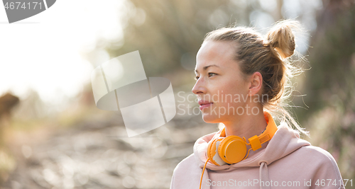 Image of Portrait of beautiful sports woman with hoodie and headphones during outdoors training session.