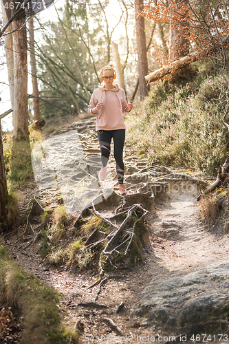 Image of Active sporty woman listening to the music while running in autumn fall forest. Female runner training outdoor. Healthy lifestyle image of young caucasian woman jogging outside