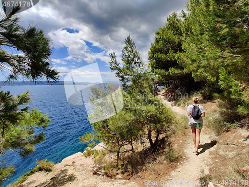 Image of Young active feamle tourist wearing small backpack walking on coastal path among pine trees looking for remote cove to swim alone in peace on seaside in Croatia. Travel and adventure concept