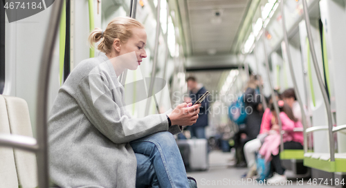 Image of Portrait of lovely girl typing message on mobile phone in almost empty public subway train. Staying at home and social distancing recomented due to corona virus pandemic outbreak