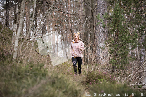 Image of Active sporty woman listening to the music while running in autumn fall forest. Female runner training outdoor. Healthy lifestyle image of young caucasian woman jogging outside