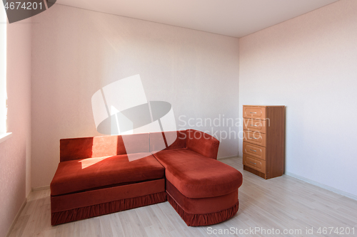 Image of The interior of a room that was empty before the move, there is a sofa and a chest of drawers in the room